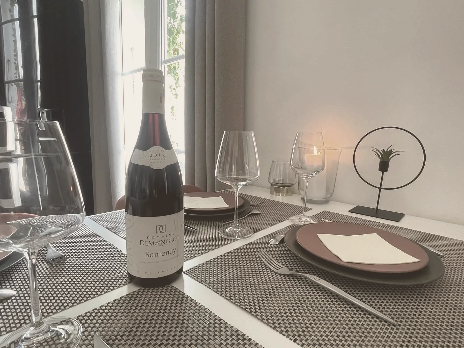 Table dressée aux Capucines : verres fins, bougie allumée et lumière douce d'une fenêtre ouverte