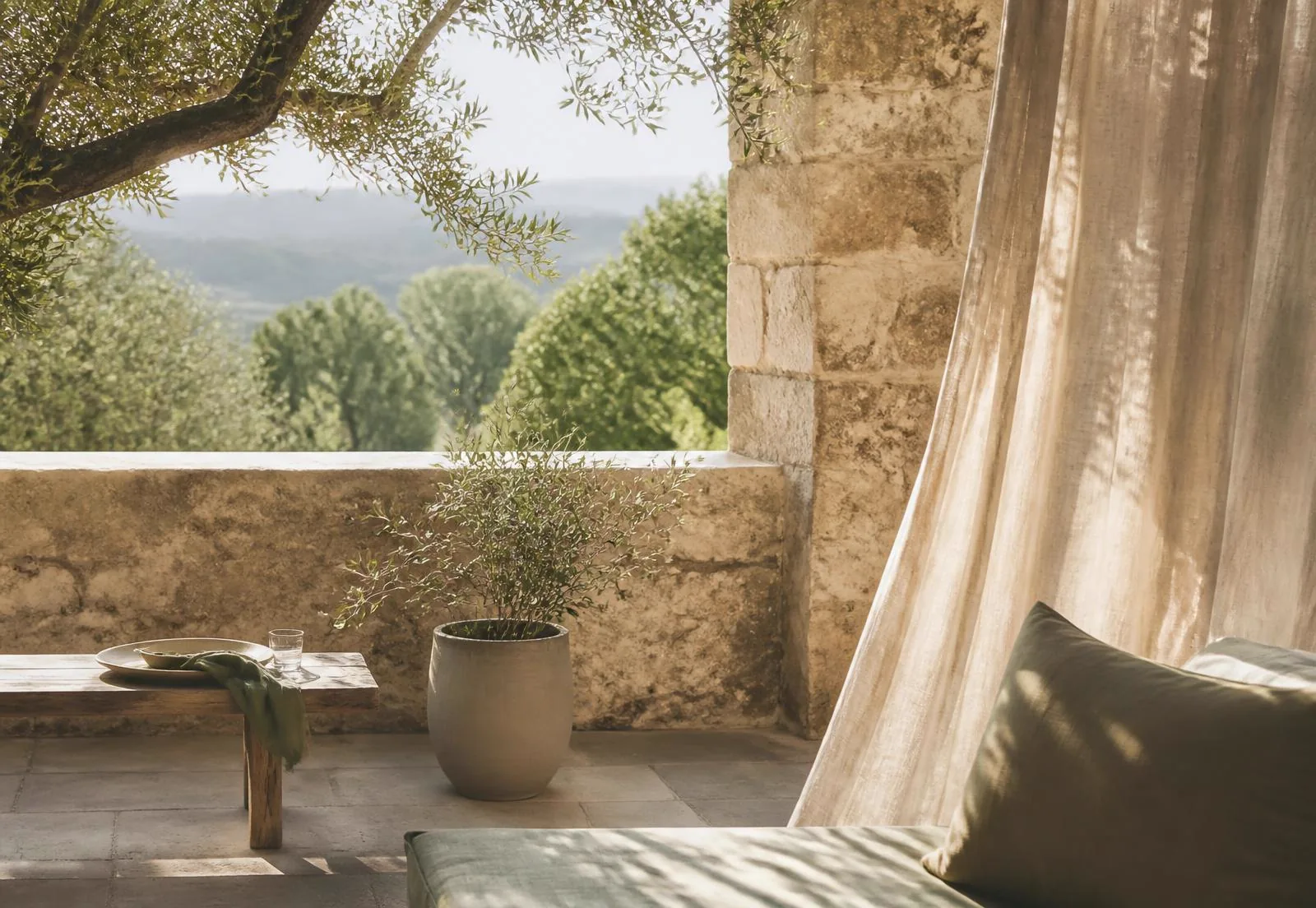 Terrasse en pierre baignée de lumière, oliviers et rideau de lin en Ardèche
