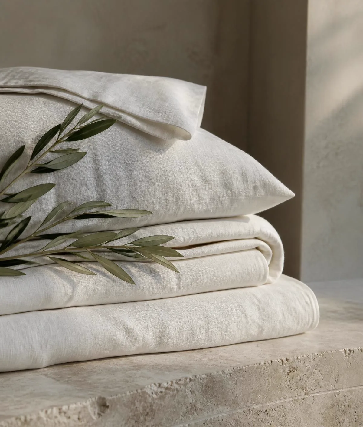 Linge de maison en lin soigneusement plié et rameau d'olivier